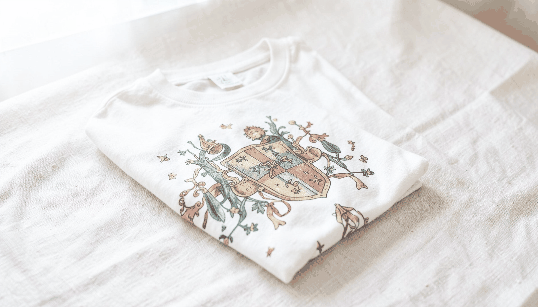 A folded graphic t-shirt with a playful medieval-inspired print, resting on a light linen background with soft natural daylight from a nearby window.