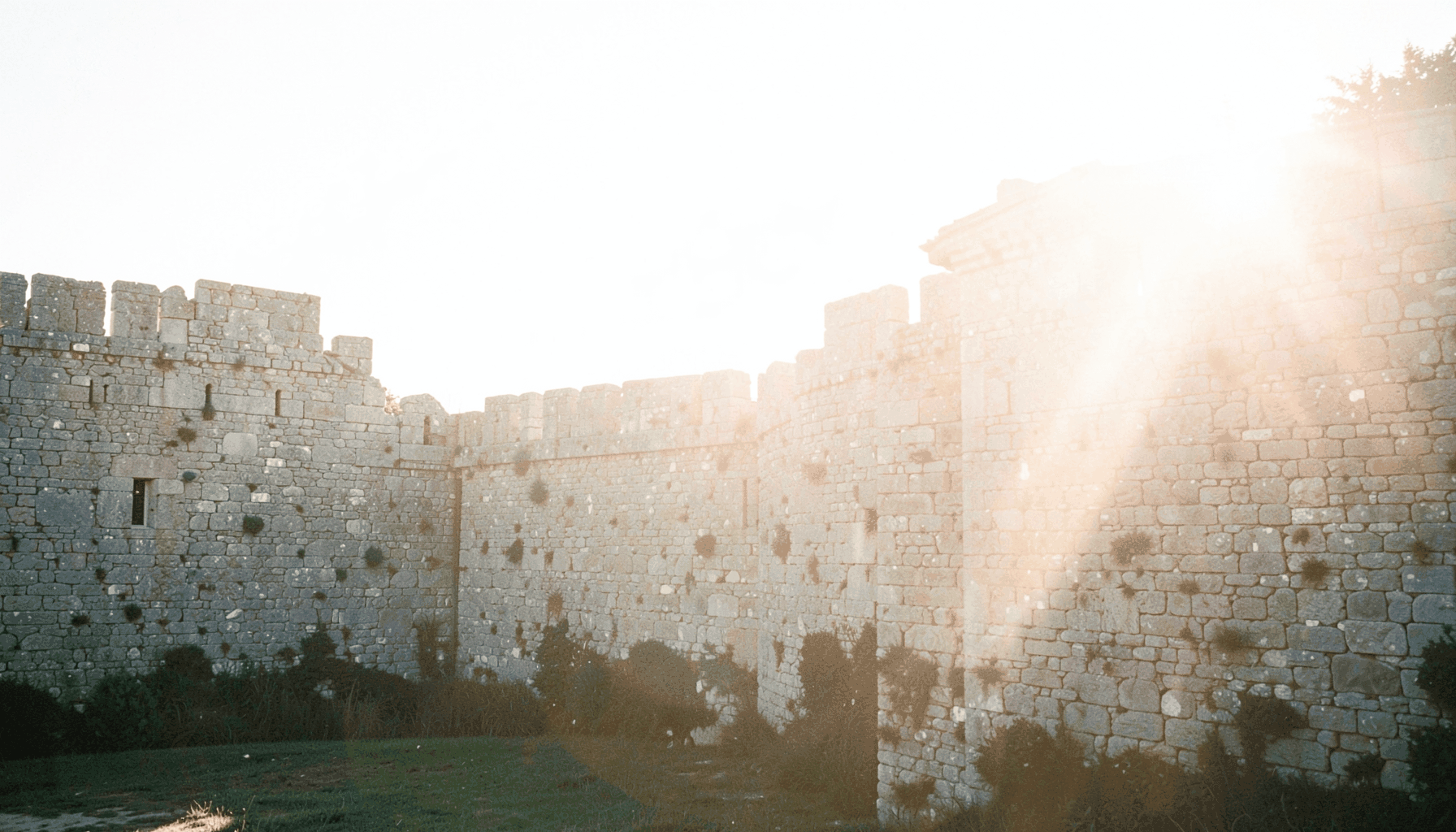 A cinematic wide shot of a stone castle wall bathed in golden-hour light, with a faint lens flare suggesting an epic film atmosphere