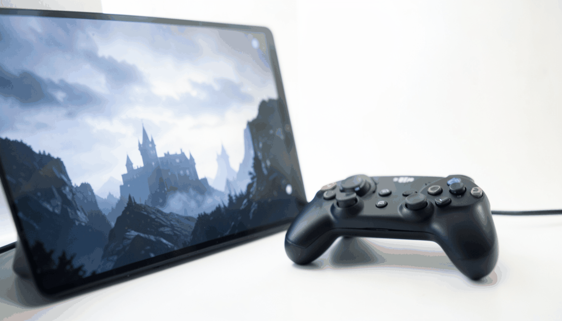 A gaming controller resting beside a glowing screen showing a dark medieval landscape with castle silhouettes, moody and atmospheric