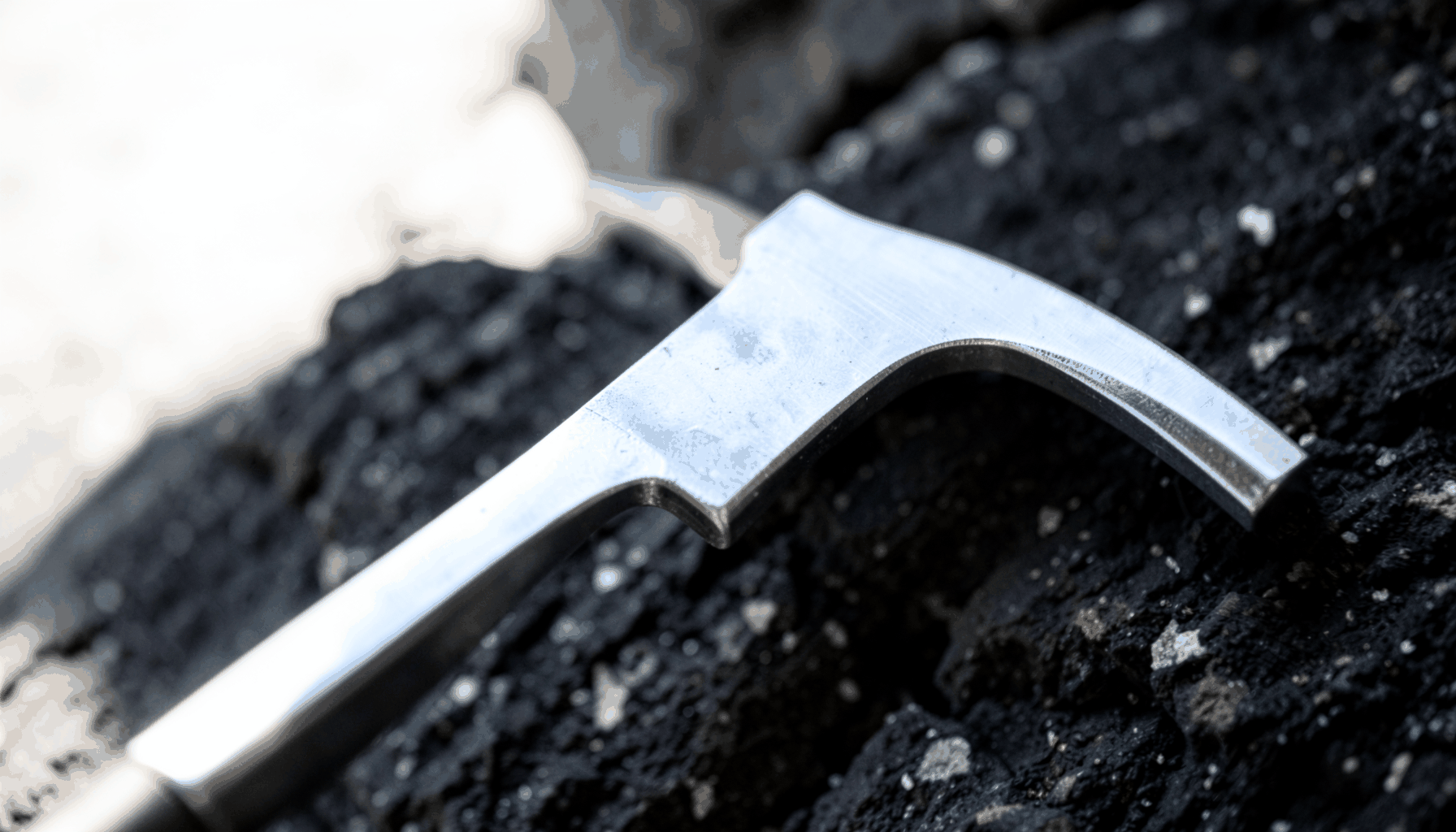 A close-up of a polished steel poleaxe head against a dark stone background, dramatic side lighting emphasising the blade's edge and hammer face